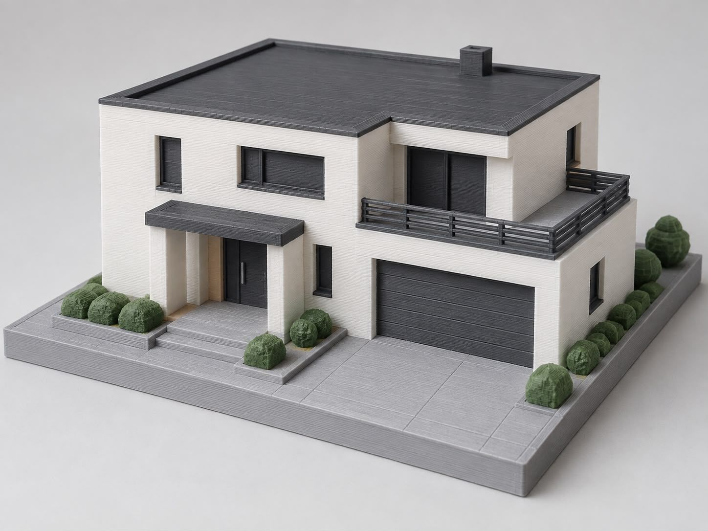 Weißes Hausmodell einer modernen Stadtvilla mit dunklem Flachdach, Balkon und Doppelgarage auf grauer Grundplatte
